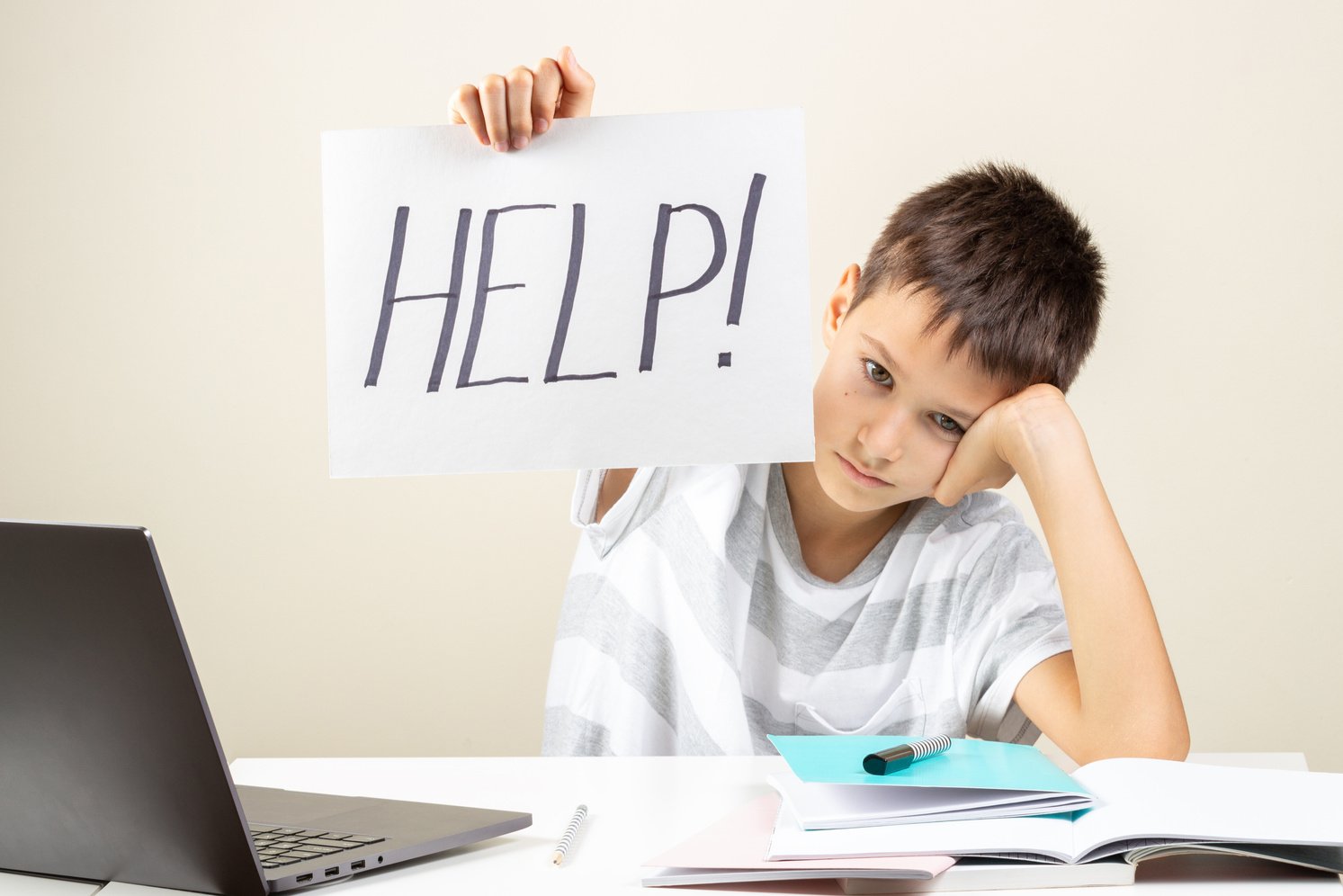 Learning Difficulties, School, Education, Online Remote Learning Concept. Tired Frustrated Boy Sitting at Table and Holding Card with Word Help