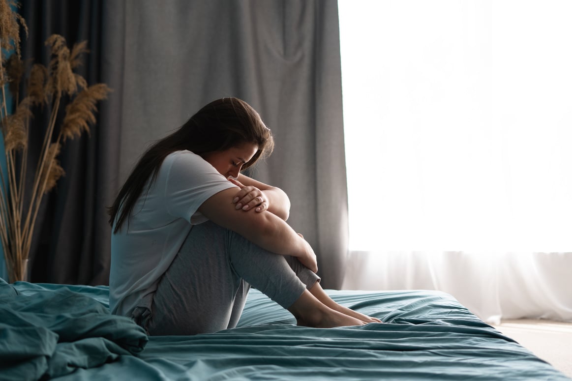 Sad woman sitting on bed in bedroom with light from window. Abuse concept